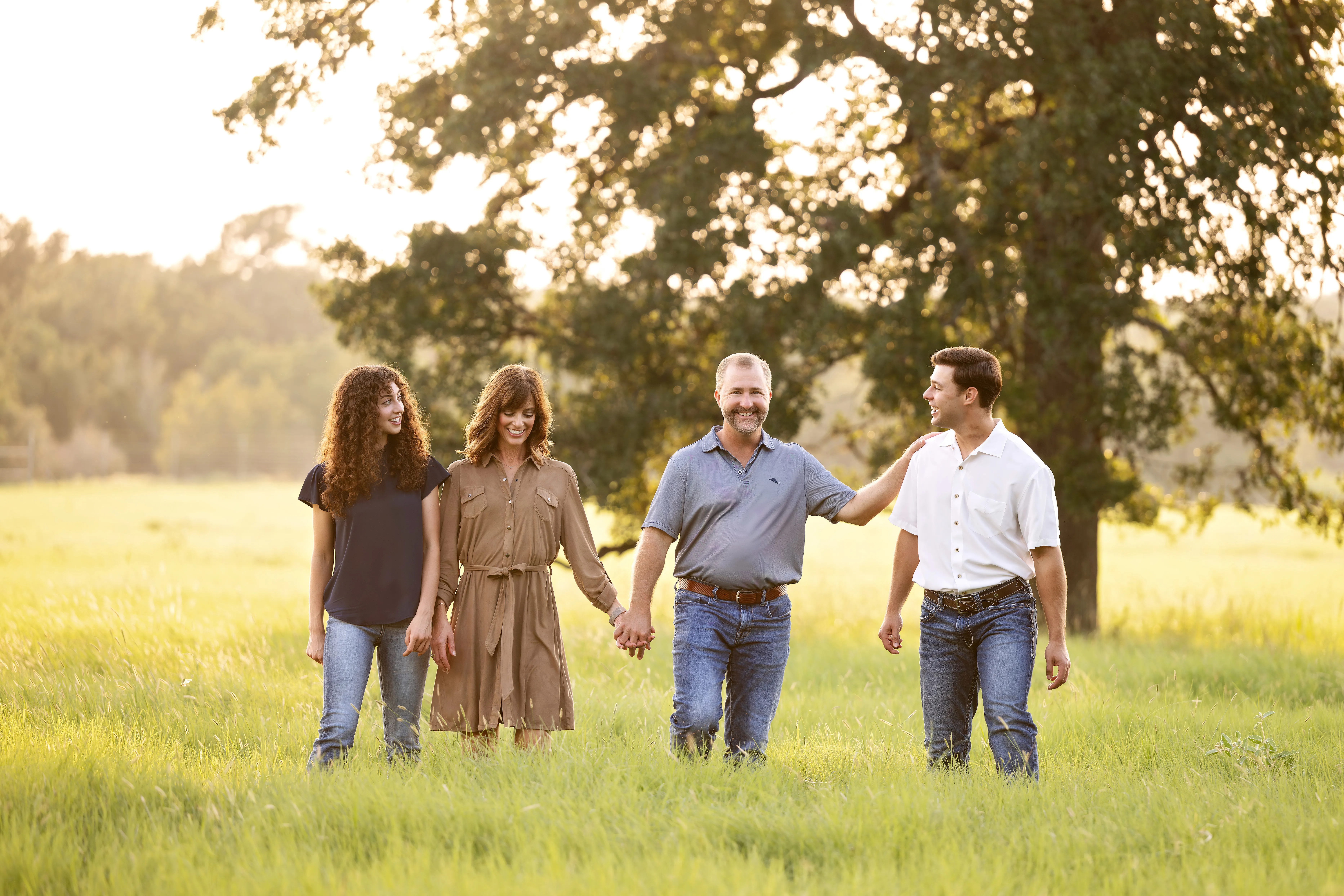 A smiling family of four walks in the grass.